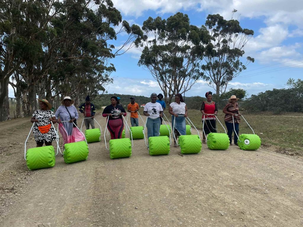 A group of individuals on a dirt road, each using green, wheeled agricultural tools, promoting community farming and sustainable practices.