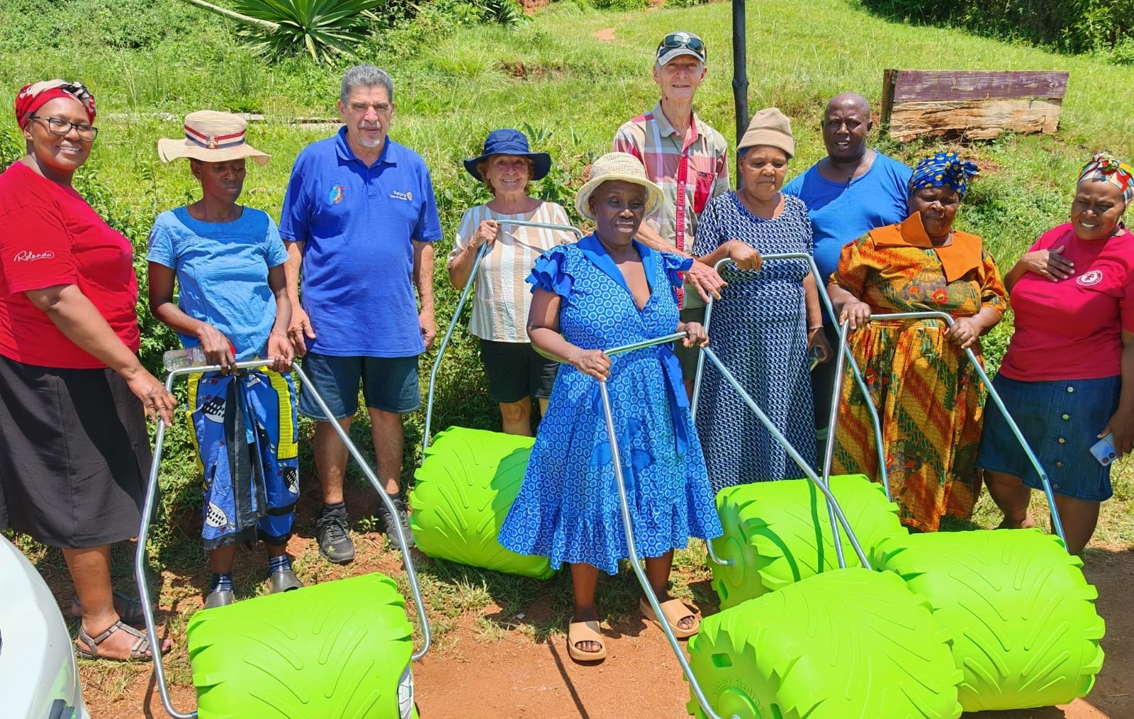 A group of diverse individuals, including women and men, poses with green farming equipment outdoors, showcasing community engagement and agricultural innovation.