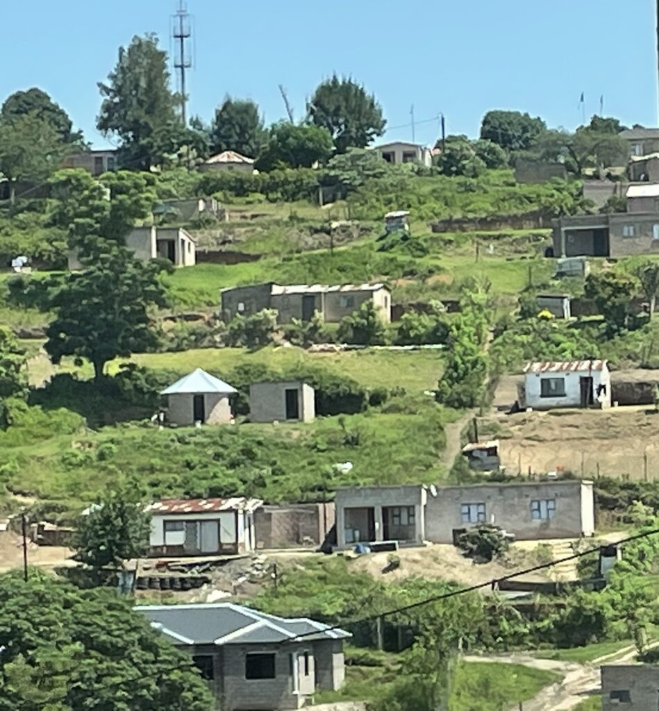 Hillside village with various houses arranged among green vegetation. A mobile tower is visible in the background, highlighting rural development.