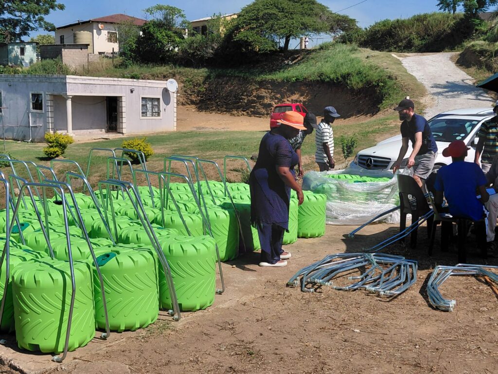 Community members organize bright green containers and equipment outside a building, indicating preparations for a local project or initiative.
